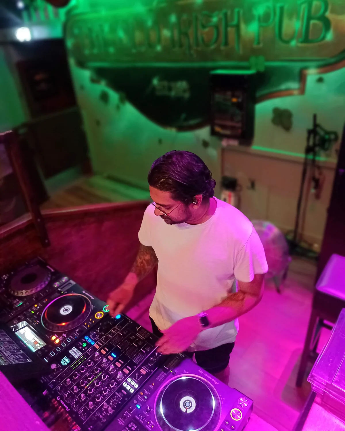 Rasmus bag DJ-pulten i en pub i grønt og lyserødt lys